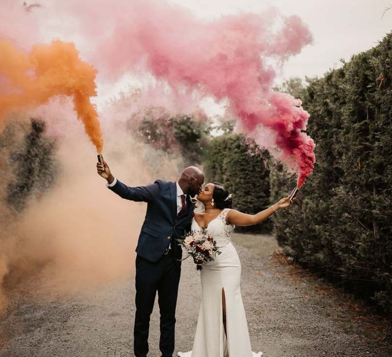 Bride and groom holding pink and orange smoke flares at The Old Kent Barn wedding venue