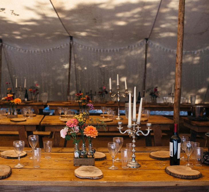 Rustic Wooden Tables | White Tapered Candles | Silver Candlestick Holders | Log Slice Place Settings | Bright Flowers in Glass Bottles | White Bunting | Macrame Decor, Vintage Caravan Photobooth and Five-Tier Naked Wedding Cake for Boho Wedding in Woodlands | Freckle Photography