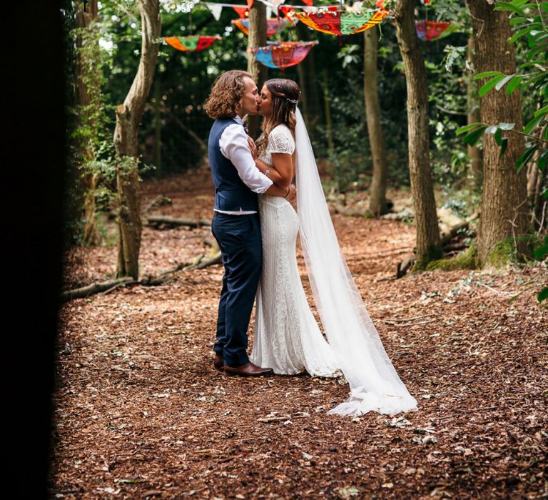 Bride in Lenora Dress by Wtoo Watters with Lace Cap Sleeves and Keyhole Back | Groom in Blue Waistcoat and Trousers with Colourful Patterned Bow Tie | Colourful Bunting | Hanging Upside Down Umbrellas | Macrame Decor, Vintage Caravan Photobooth and Five-Tier Naked Wedding Cake for Boho Wedding in Woodlands | Freckle Photography