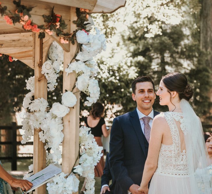 Outdoor Home Wedding Ceremony with Bride in Pronovias Danaia Wedding Dress and Groom in Navy Moss Bros. Suit