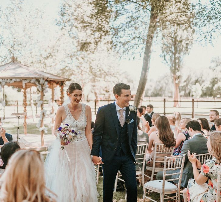 Bride in Pronovias Danaia Wedding Dress and Groom in Navy Moss Bros. Suit Walking up the Aisle Just Married