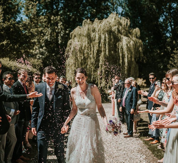 Happy Confetti Moment with Bride in Pronovias Danaia Wedding Dress and Groom in Navy Moss Bros. Suit