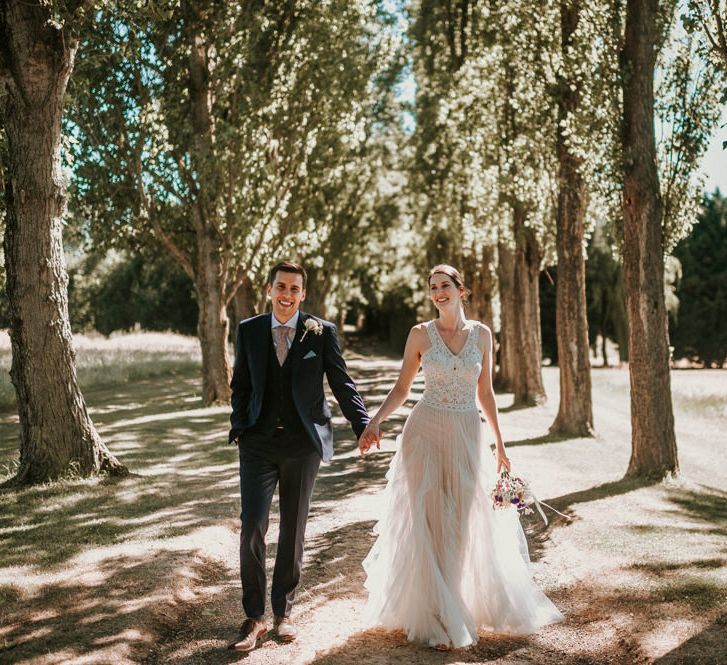 Bride in Pronovias Danaia Wedding Dress and Groom in Moss Bros. Suit Holding Hands in the Woods