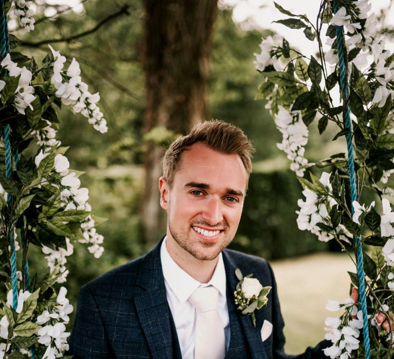 Groom in Navy Check Moss Bros. Suit Sitting on Ivy Covered Swing