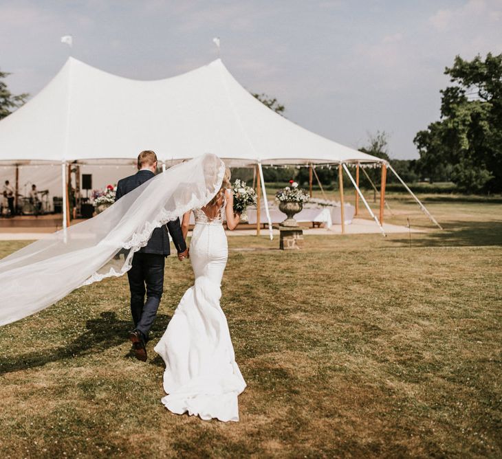 Bride in Pronovias Wedding Dress and Groom in Moss Bros Suit Walking Towards Tent Reception