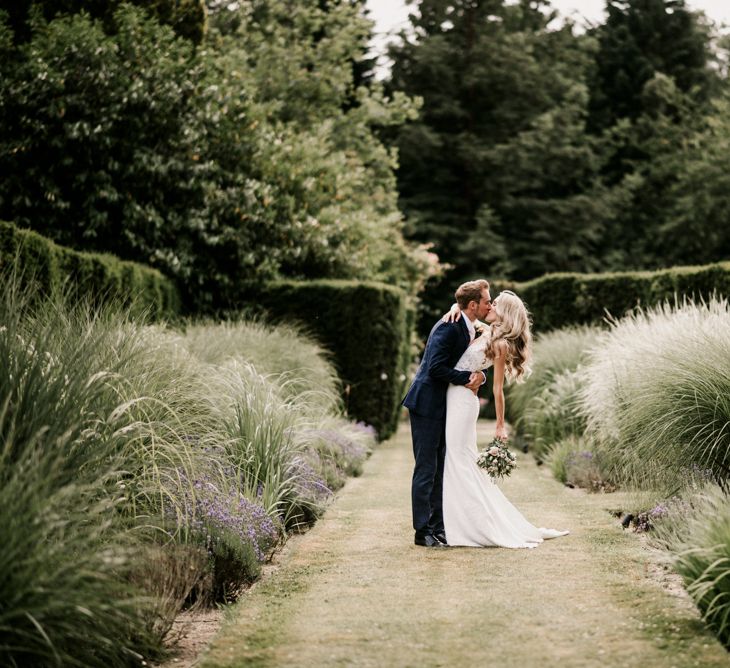 Bride in Vicenta Pronovias Wedding Dress and Groom in Navy Check Moss Bros Suit Kissing