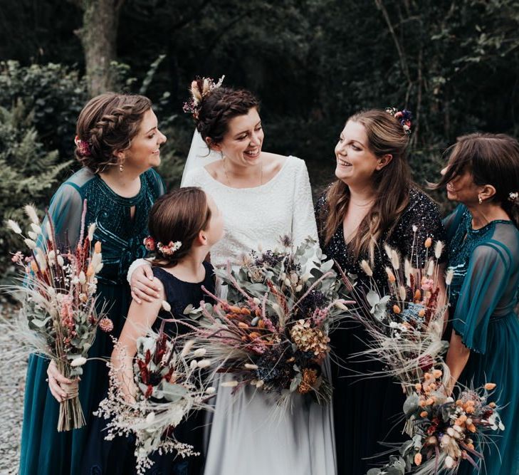 Bridal Party Laughing in the Woods with Bridesmaids in Emerald Green &amp; Navy Dresses Holding Dried Flower Bouquets