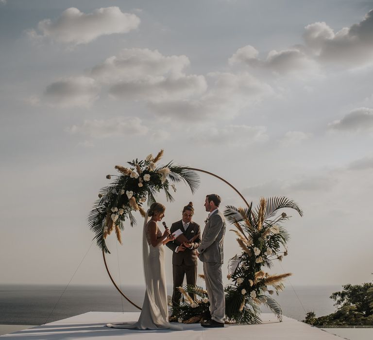 Bride and groom during intimate Thailand wedding ceremony with amazing views and moon gate decor and pampas grass