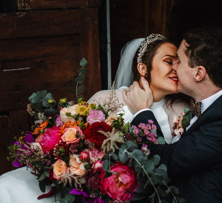 Groom Kissing His Bride Whilst Holding a Pink Wedding bouquet