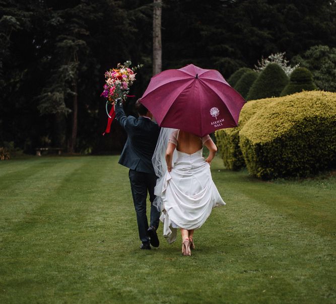 Bride and Groom Walking Under an Umbrella at their Askham Hall Wedding