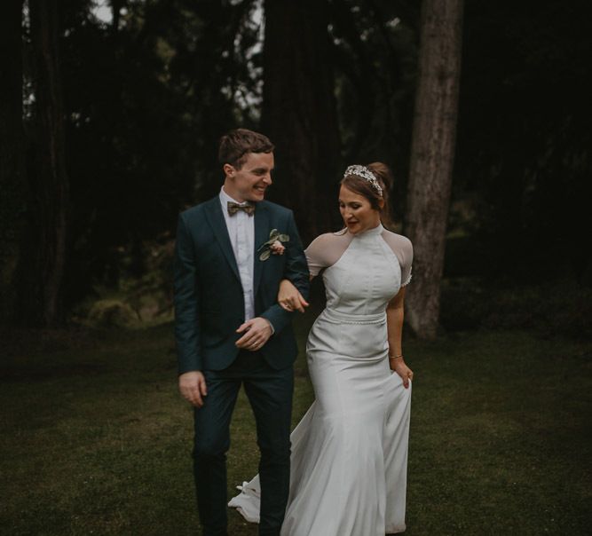 Bride in Bespoke Wedding Dress with Cap Sleeves and Bridal Crown and Groom in Navy Suit and Bow Tie