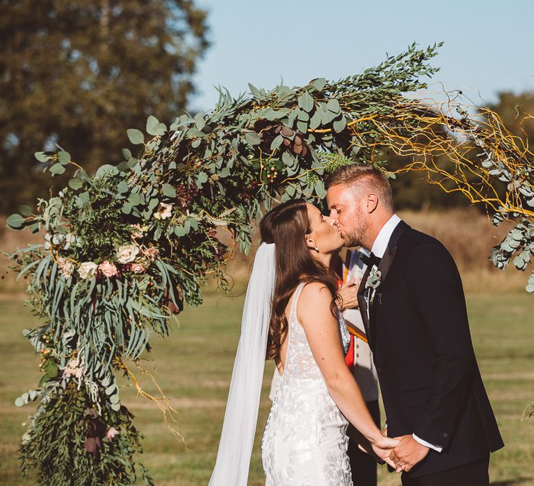 Bride and groom say 'I do' with foliage hoop decor for intimate outdoor ceremony