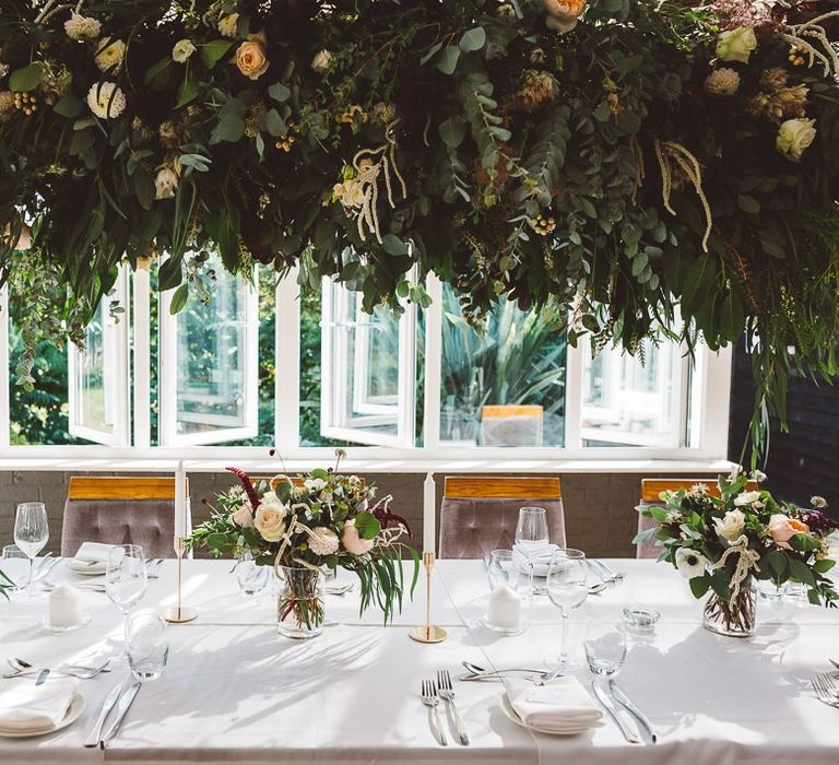 Hanging foliage and floral table arrangements styled with gold candlesticks for intimate and romantic wedding