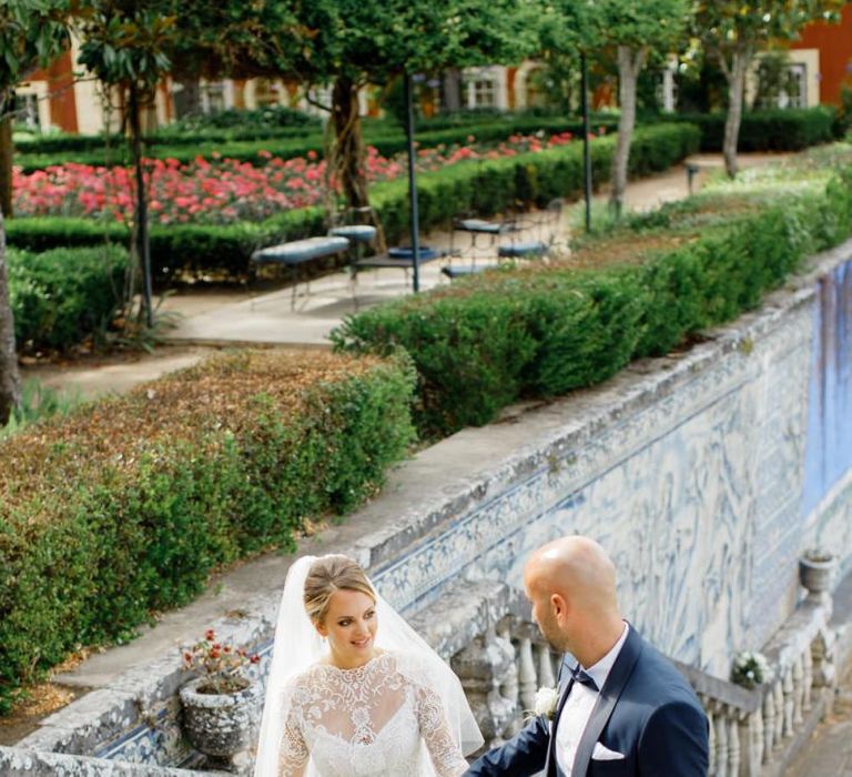 Groom in Navy Tuxedo Helping His Bride in a Long Sleeve Wedding Dress up the Steps