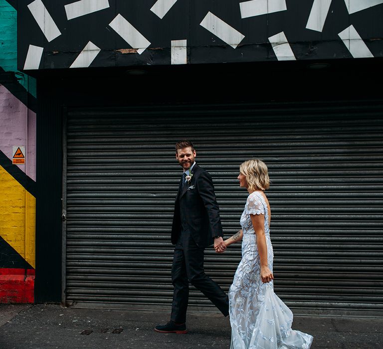 Stylish Bride in Lace Hermione De Paula Wedding Dress and Groom in Ted Baker Suit Walking Through East London