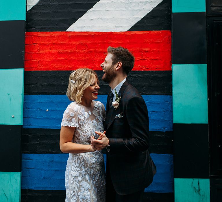 Bride in Lace Hermione De Paula Wedding Dress and Groom in Ted Baker Suit Standing in Front of Street Art