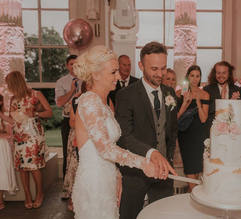 Bride in Suzanne Neville wedding dress cuts wedding cake with groom