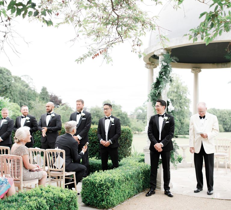 Groomsmen in black tie suits at outdoor ceremony