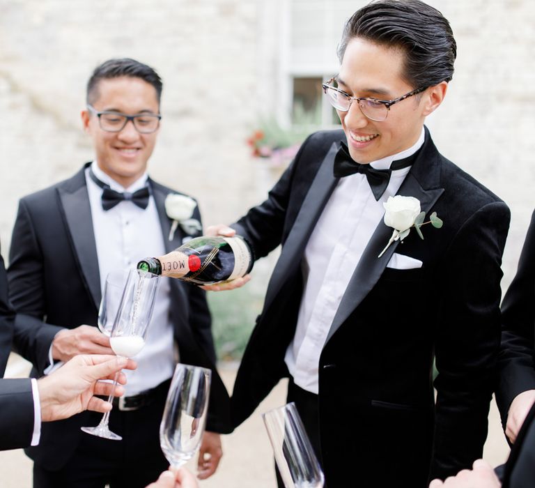 Groomsmen in black tie suits drinking champagne on wedding morning