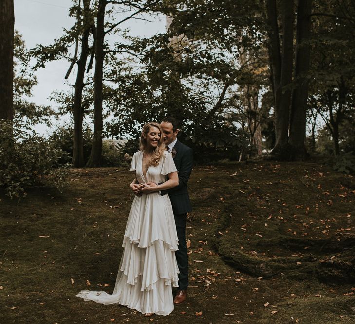 Bride in Tiered Houghton NYC Wedding Dress and Groom in Check House of Fraser Suit Cuddling in a Forest