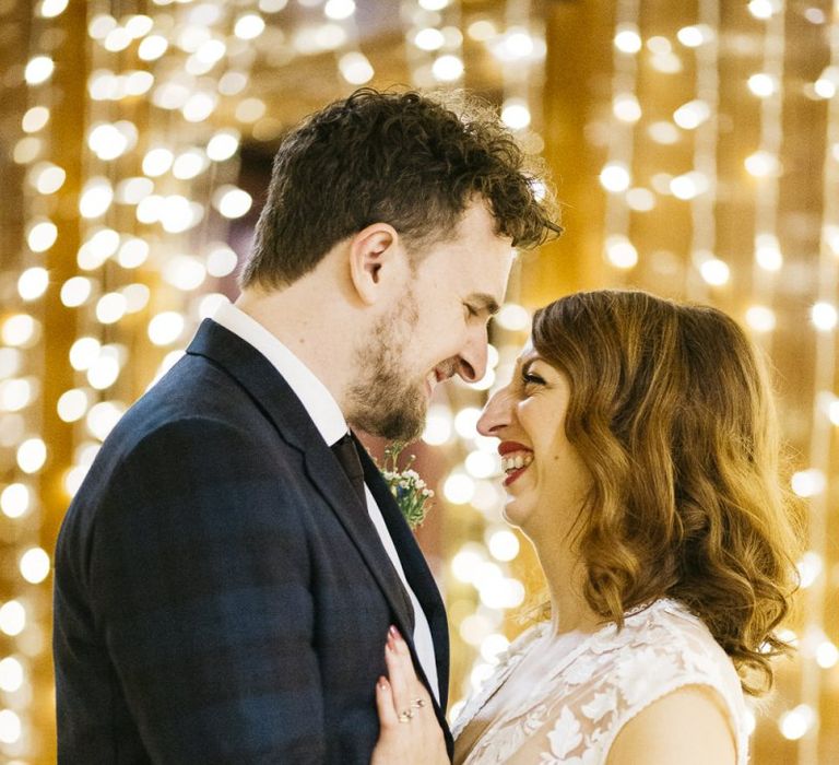 Bride and groom embrace with fairy-light backdrop