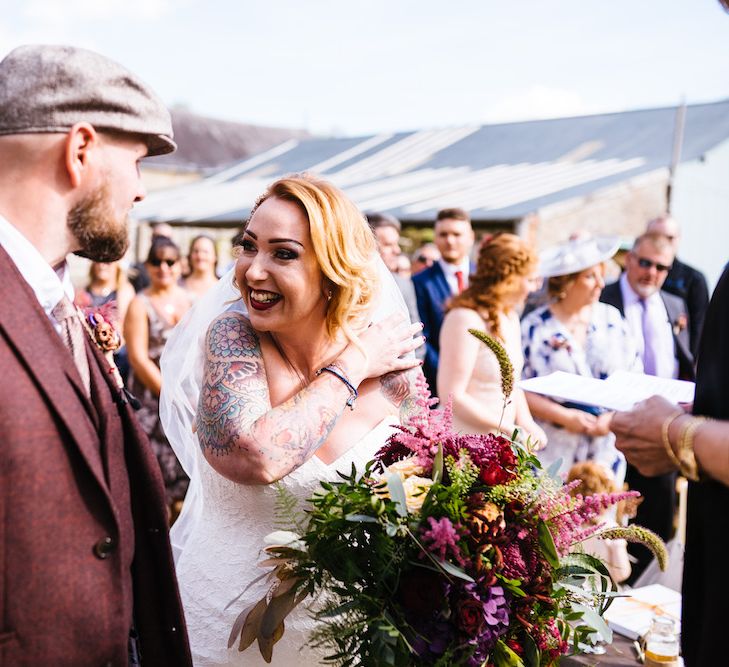 Wedding Ceremony | Bride in Strapless Sassi Holford Wedding Dress with Sweetheart Neckline | Groom in Burgundy Tweed Three Piece Suit | Bright Bouquet | Edison Bulb Floral Installation at Kingsthorpe Lodge Barn Wedding | Johnny Dent Photography