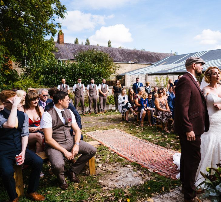 Wedding Ceremony | Bride in Strapless Sassi Holford Wedding Dress with Sweetheart Neckline | Groom in Burgundy Tweed Three Piece Suit | Edison Bulb Floral Installation at Kingsthorpe Lodge Barn Wedding | Johnny Dent Photography