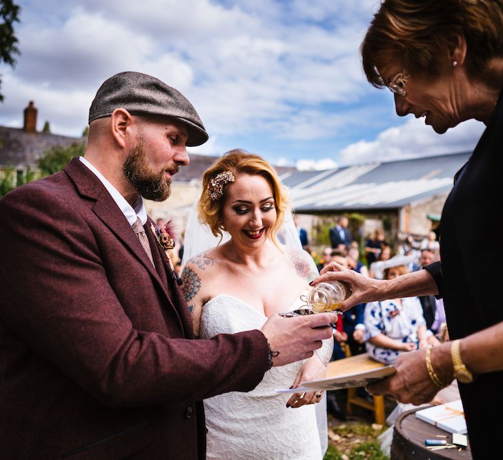 Wedding Ceremony | Bride in Strapless Sassi Holford Wedding Dress with Sweetheart Neckline | Groom in Burgundy Tweed Three Piece Suit | Edison Bulb Floral Installation at Kingsthorpe Lodge Barn Wedding | Johnny Dent Photography