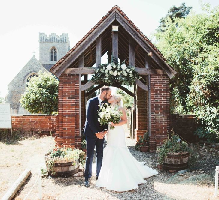 Just Married Kiss | Bride in Essense of Australia Dress with Spaghetti Straps and Fishtail | Floor Length Veil | Bridal Bouquet of White Flowers and Greenery | Groom in Blue Suit with White and Green Buttonhole | Quintessential English Country Wedding in Glass Marquee at Family Home | Maryanne Weddings Photography