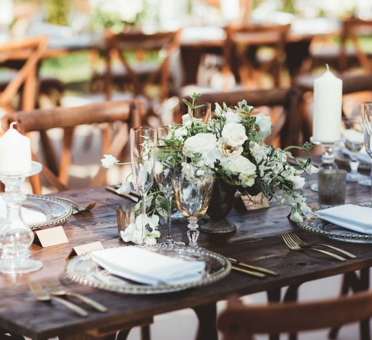 Long Wooden Farm Table | Wooden Cross Back Chairs | Glass Charger Plates | Gold Cutlery | Gold Rimmed Glassware | Table Centrepieces of White Flowers and Greenery | White Pillar Candles | Quintessential English Country Wedding in Glass Marquee at Family Home | Maryanne Weddings Photography