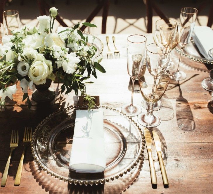 Place Setting | Glass Charger Plate | Gold Cutlery | Gold Rimmed Glassware | Table Arrangement of White Flowers and Greenery | Quintessential English Country Wedding in Glass Marquee at Family Home | Maryanne Weddings Photography