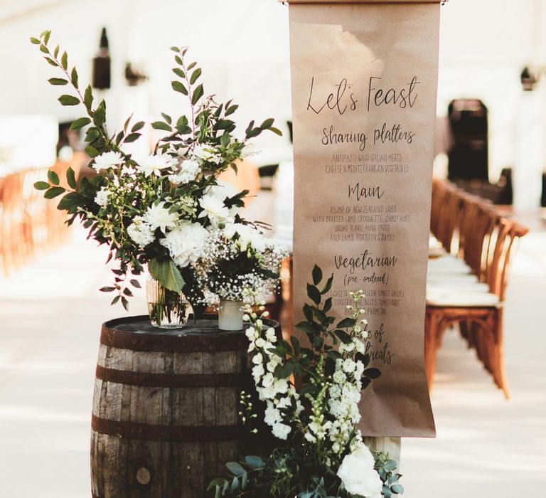 Wedding Breakfast Menu in Calligraphy on Kraft Paper | Wooden Barrel | Large Glass Vases  of White Flowers and Eucalyptus | Quintessential English Country Wedding in Glass Marquee at Family Home | Maryanne Weddings Photography