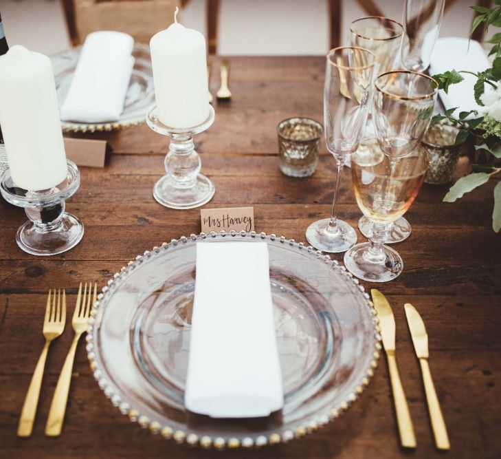 Place Setting | Glass Charger Plates | Gold Cutlery | Gold Rimmed Glassware | White Pillar Candles | Glass Candlesticks | Calligraphy Name Cards | Quintessential English Country Wedding in Glass Marquee at Family Home | Maryanne Weddings Photography