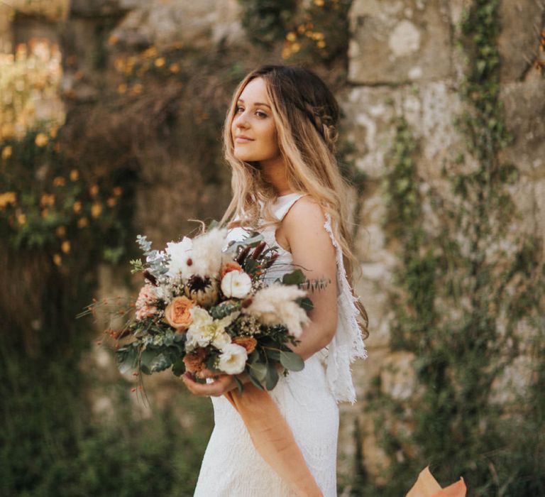 Boho Bride with Half Up Half Down Braided Hair Holding a Bouquet with Pampas Grass and Coral Flowers Tied in Ribbon