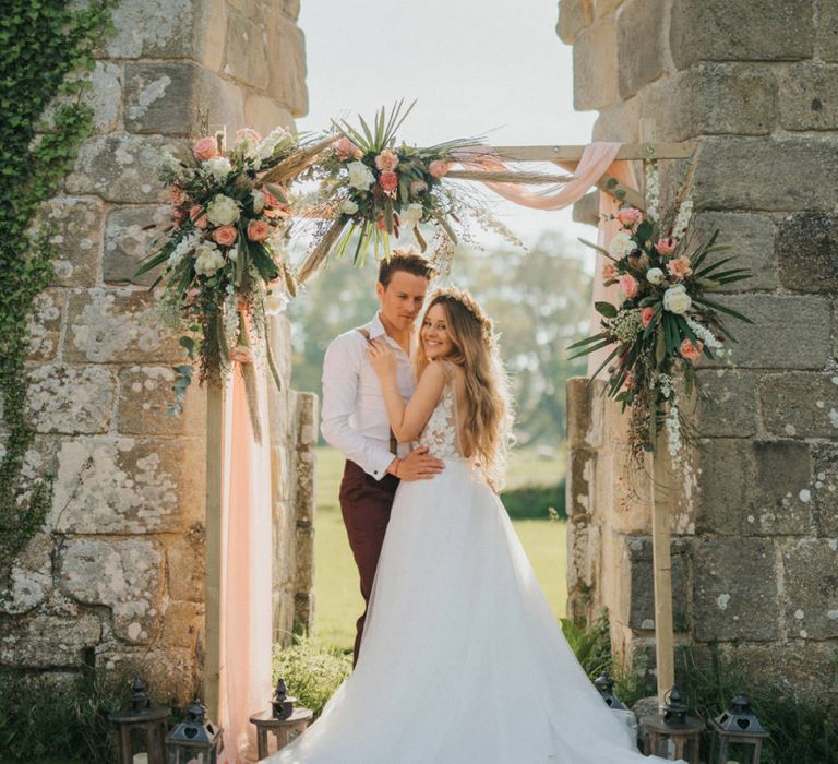 Boho Bride and Groom Standing in Front of a Wooden Altar Covered in Flowers