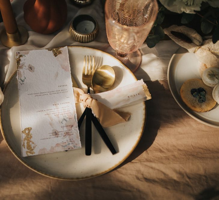 Elegant Place Setting with Gold and Black Cutlery Tied with Ribbon and Menu Cards