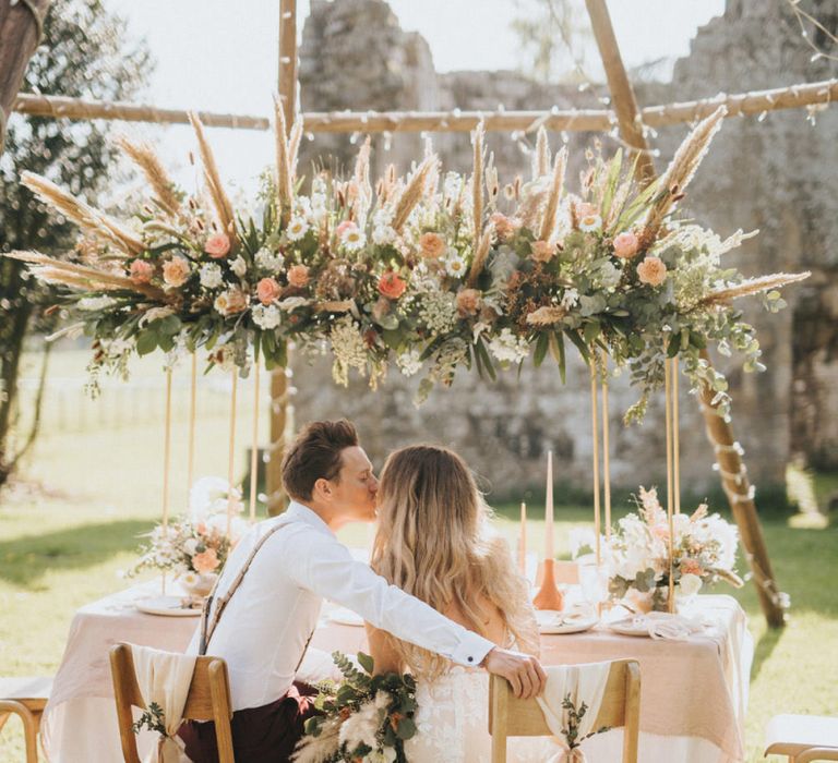 Boho Bride and Groom Kissing at Their Tablescape Under a Naked Tipi