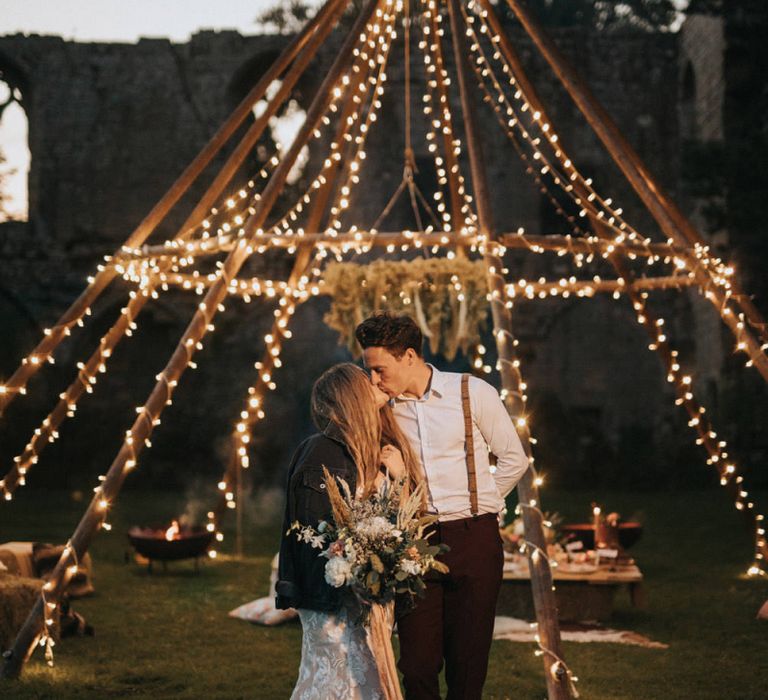 Boho Bride and Groom Standing in Front of Light Covered Naked Tipi