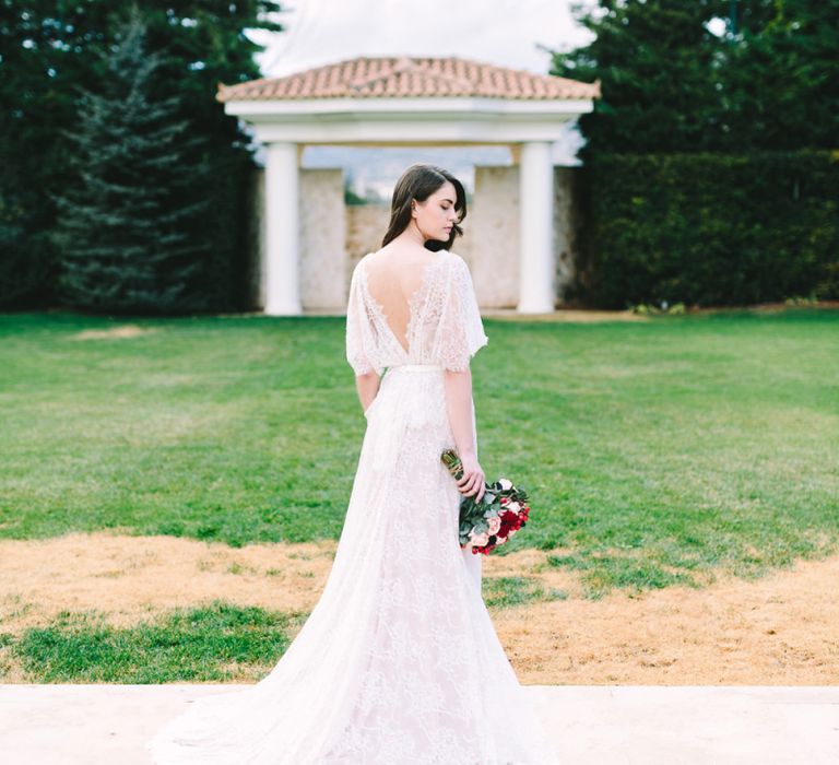 Bride in Lace Wedding Dress with Low Back Detail Holding a Red Wedding Bouquet