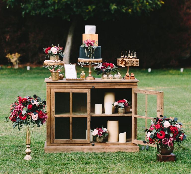 Wooden Dessert Table with Individual Cakes and Treats Surrounded by Floral Arrangement and Candles