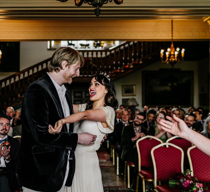 Wedding Ceremony at Walcot Hall with Bride in Vintage  Wedding Dress with Gold Trims and Groom in Velvet Blazer Laughing