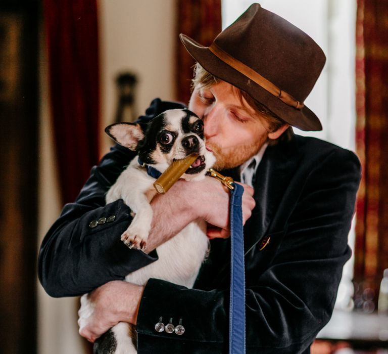 Groom in Navy Blue Velvet Blazer and Hat Hugging His Pet Dog