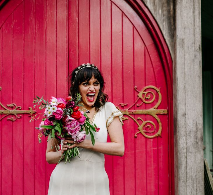 Happy Bride in Vintage Wedding Dress with Batwing Sleeves Holding a Red and Pink Floral Bouquet