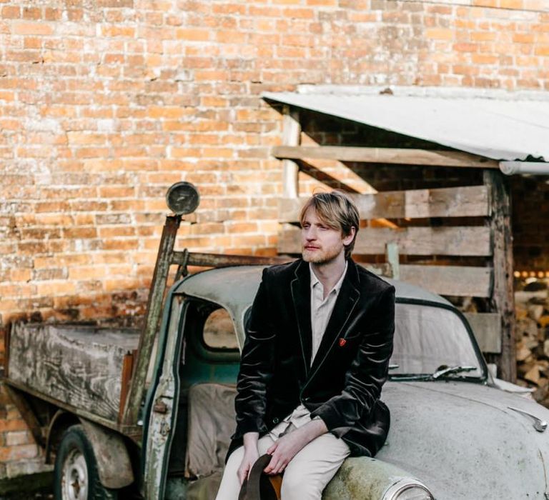 Groom in Navy Velvet Blazer and Hat Sitting on an Old Truck