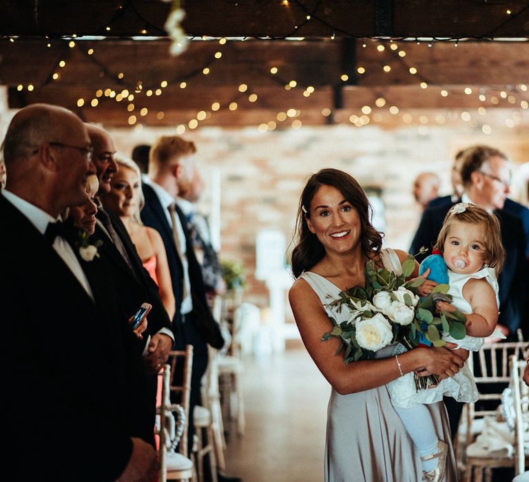 Bridesmaid carries flower girl down the aisle