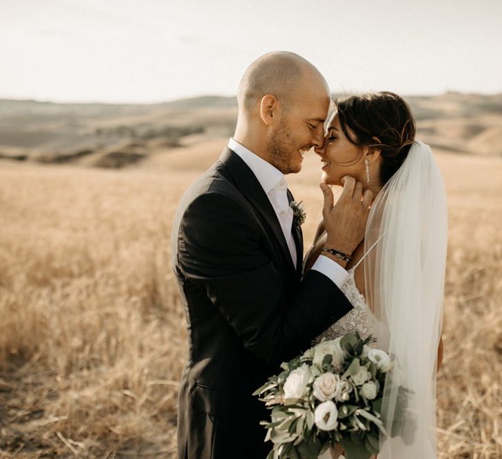 Bride wears Justin Alexander wedding dress with white flower bouquet and  groom in black suit