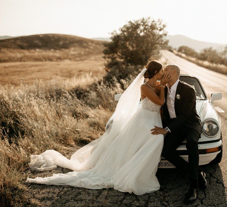 Bride wears Justin Alexander wedding dress with groom in black suit and white wedding car