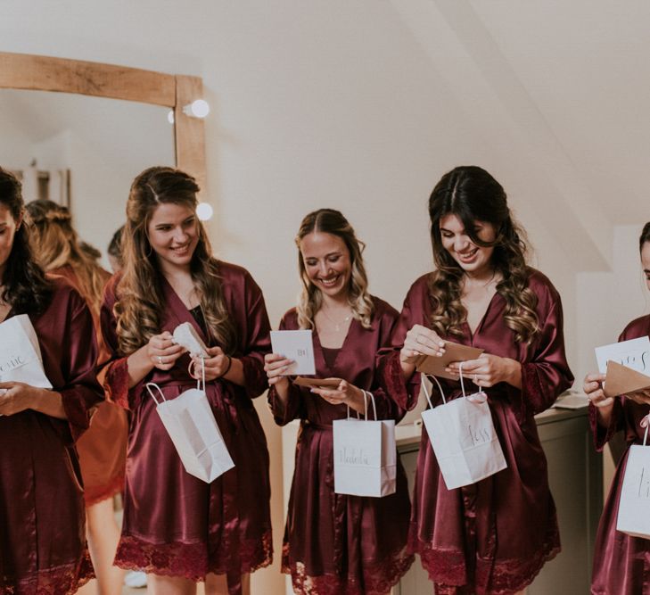 Bridesmaids in Matching burgundy Robes Opening Their Bridesmaid Gift Bags | Millbridge Court, Surrey Wedding with DIY Decor, Foliage &amp; Giant Balloons | Nataly J Photography