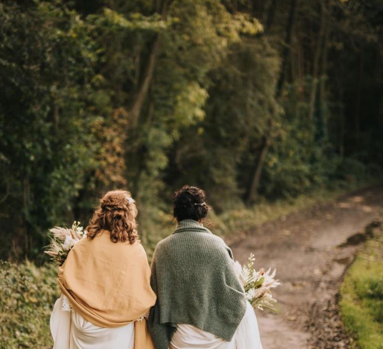 Two Brides Walking Through the Woods with Blankets Wrapped Around Them