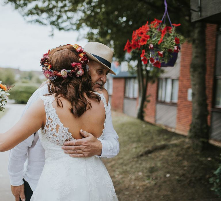 Bride in Lace Wedding Dress with Bright Flower Crown and Wedding Bouquet Embracing the Father of the Bride